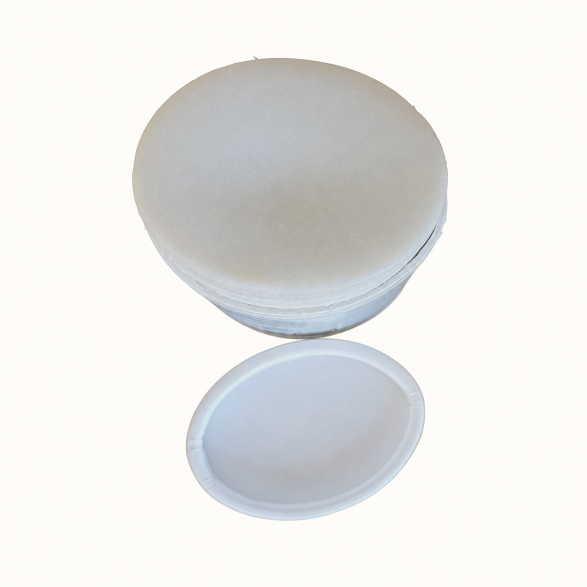 A white circular tube of deodorant with its matching lid resting below it, isolated on a solid white background.